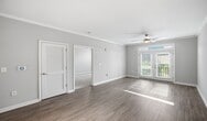 This 670-square-foot, one-bedroom, one-bathroom apartment — Design 1C Premier 2 #443 — is located at 141 Park at North Hills St in Raleigh, NC. The single-floor layout is thoughtfully designed to maximize space and comfort throughout. The living room features light hardwood-style flooring, crown molding, a ceiling fan, and French doors that invite abundant natural light and outdoor views. An elegant arched entryway connects the living area to the kitchen, which is outfitted with white shaker-style cabinetry, light gray subway tile backsplash, white countertops, and stainless steel appliances including a range and French door refrigerator. The 150-square-foot primary bedroom is carpeted for warmth, features crown molding and a ceiling fan, and receives natural light through a large window with wooded views. The bathroom offers hardwood-style flooring, white cabinetry with a taupe countertop, and direct access to a dedicated walk-in closet with built-in shelving. Neutral tones, consistent crown molding, and ceiling fans throughout the unit create a cohesive, polished ambiance ideal for comfortable, modern living.
