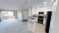 This single-floor residence offers a clean, contemporary design with a thoughtful layout that maximizes both comfort and functionality. The open-concept living and kitchen area serves as the heart of the home, where vaulted ceilings lend a sense of generous vertical space and airiness. The kitchen is well-equipped with crisp white cabinetry, gray quartz-style countertops, stainless steel appliances including a range, microwave, and refrigerator, and a peninsula with an integrated sink — ideal for both meal preparation and casual dining. Light wood-look flooring grounds the kitchen, transitioning seamlessly to soft carpeting throughout the living and bedroom areas. The spacious living room features a sliding glass door that opens to a private balcony, inviting natural light and outdoor views into the space. The bedrooms are generously sized, each with large windows fitted with blinds and plush carpeting. The primary bedroom boasts floor-to-ceiling mirrored closet doors that enhance the sense of space, with an en-suite bathroom conveniently accessible. Both bathrooms are finished in a clean, neutral palette, featuring tub-shower combinations with curved curtain rods, white tile surrounds, and updated vanities with ample counter space. Overall, the residence presents a bright, move-in-ready interior with modern finishes throughout.
