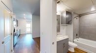 Located at 2121 S Broadway in Denver, Colorado, this single-floor unit offers a well-designed, contemporary living space with a clean, modern aesthetic throughout. The open layout is unified by warm wood-style flooring that flows seamlessly from room to room, complemented by crisp white walls and recessed lighting.

The kitchen is a standout feature, showcasing slate-gray cabinetry with brushed hardware, white quartz countertops, and a herringbone-pattern tile backsplash. Stainless steel appliances — including a refrigerator, electric range, and over-the-range microwave — complete this functional and stylish culinary space. A door at the end of the kitchen leads directly to a private balcony, filling the area with natural light and offering outdoor access.

The living area is bright and airy, with a glass-panel balcony door that invites natural light and views of the surrounding neighborhood. Two additional rooms with wood-style flooring provide versatile spaces suitable for a bedroom or home office, each featuring ceiling fixtures and clean white walls.

The bathroom is finished with gray cabinetry, a white vanity countertop, a wall-mounted medicine cabinet, and a tiled shower enclosure. A ventilation unit above ensures comfort and functionality. Overall, the unit presents a cohesive, modern design ideal for urban Denver living.