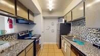 This single-floor residence offers a practical and functional layout designed for comfortable everyday living. The galley-style kitchen is a standout feature, lined on both sides with gray cabinetry, granite-look countertops, and stainless steel appliances including a refrigerator and electric range. A decorative mosaic tile backsplash adds visual interest, while light tile flooring runs throughout the space, providing a clean and cohesive look.

Adjacent to the kitchen, an open pass-through connects to a casual dining or living area, brightened by recessed overhead lighting and a neutral color palette. The open layout creates a welcoming flow between spaces, with light tile flooring continuing seamlessly underfoot.

The bedrooms are generously proportioned with large windows that invite natural light and offer views to the exterior. Neutral gray walls and textured ceilings complement the bright tile floors, creating a calm and airy atmosphere in each room.

The bathroom is well-appointed, featuring a granite-topped vanity with an undermount sink, a full bathtub with a tiled surround, and a textured ceiling. Additional utility is provided by a climate control thermostat and ceiling ventilation, ensuring year-round comfort throughout the residence.