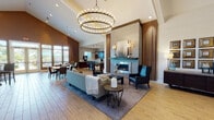 Located at 13968 John Humphrey Drive in Orland Park, Illinois, this single-floor community space is designed with a refined, contemporary aesthetic that balances comfort and functionality. The expansive open-plan layout encompasses multiple distinct zones, all unified by warm hardwood-style flooring, soaring vaulted ceilings, and a cohesive neutral-and-teal color palette.

The central gathering area is anchored by a striking floor-to-ceiling tile fireplace surround, flanked by wall sconces and complemented by a dramatic double-ring chandelier overhead. Plush seating arrangements invite relaxed conversation, while a dedicated lounge near large floor-to-ceiling windows offers direct access to an outdoor patio, flooding the interior with natural light and outdoor views.

A fully equipped kitchen features rich dark cabinetry, subway tile backsplash, stainless steel appliances including a wall oven, and an illuminated breakfast bar with stylish pendant lighting. An adjacent dining area with a solid wood table and leather seating sits beside expansive windows overlooking the outdoor space.

Additional areas include a billiards room and supplementary seating vignettes, making this a versatile, well-appointed destination for gathering and recreation.