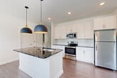 Located at 5740 Buffington Rd in Union City, GA, this well-appointed 2-bedroom, 2-bathroom single-story home offers a clean, modern aesthetic with thoughtfully selected finishes throughout. The open-concept kitchen and living area serves as the heart of the home, featuring a central island with a striking dark granite countertop, an undermount sink with a brass-finish faucet, and a pair of bold navy and gold pendant lights overhead. White shaker-style cabinetry lines the kitchen walls, complemented by a classic subway tile backsplash and a full suite of stainless steel appliances. Wood-look plank flooring flows seamlessly through the kitchen and living areas, adding warmth and continuity. The living room is bright and airy, with multiple windows dressed in horizontal blinds that invite natural light and outdoor views of the surrounding greenery. Each bedroom offers a comfortable, quiet retreat — the primary bedroom features wood-look flooring and a ceiling fan, while the second bedroom is finished with plush carpeting, a ceiling fan, and a window overlooking the landscape. The two bathrooms continue the home's refined palette, with dark granite vanity tops, white cabinetry, and a tub-shower combination. Two dedicated closets provide ample storage throughout.
