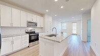 This well-appointed single-floor residence showcases a clean, modern design throughout. The heart of the home is an open-concept kitchen that flows seamlessly into the living area, creating a bright and functional space ideal for everyday living and entertaining. The kitchen is fully equipped with stainless steel appliances — including a refrigerator with ice maker, electric range, over-the-range microwave, and dishwasher — all complemented by crisp white shaker-style cabinetry and granite countertops. A central island with a built-in sink provides additional prep space and serves as a natural gathering point. Light hardwood-style flooring extends throughout the kitchen and living areas, enhancing the airy, open feel. The living room benefits from abundant natural light through windows and a glass-paneled exterior door. The bedroom features plush wall-to-wall carpeting, a ceiling fan with light fixture, and a window with exterior views, offering a comfortable and quiet retreat. The bathroom is finished with a wide granite-topped vanity, white cabinetry, a large mirror, and a tub-shower combination. Recessed lighting throughout the space adds a polished, contemporary touch, while the neutral white palette creates a clean and versatile backdrop.