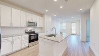 This well-appointed single-floor residence showcases a clean, modern design throughout. The heart of the home is an open-concept kitchen that flows seamlessly into the living area, creating a bright and functional space ideal for everyday living and entertaining. The kitchen is fully equipped with stainless steel appliances — including a refrigerator with ice maker, electric range, over-the-range microwave, and dishwasher — all complemented by crisp white shaker-style cabinetry and granite countertops. A central island with a built-in sink provides additional prep space and serves as a natural gathering point. Light hardwood-style flooring extends throughout the kitchen and living areas, enhancing the airy, open feel. The living room benefits from abundant natural light through windows and a glass-paneled exterior door. The bedroom features plush wall-to-wall carpeting, a ceiling fan with light fixture, and a window with exterior views, offering a comfortable and quiet retreat. The bathroom is finished with a wide granite-topped vanity, white cabinetry, a large mirror, and a tub-shower combination. Recessed lighting throughout the space adds a polished, contemporary touch, while the neutral white palette creates a clean and versatile backdrop.