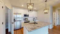 Located at 6480 Alexander Clay in Columbus, Ohio, this well-appointed single-floor home offers a thoughtfully designed layout with modern finishes throughout. The open-concept kitchen serves as the heart of the home, showcasing a large center island topped with granite countertops and an integrated sink with a matte black faucet. Crisp white shaker-style cabinetry lines the walls, complemented by a subtle tile backsplash and a full suite of stainless steel appliances. Striking geometric pendant lights in a bronze finish hang above the island, adding a contemporary touch. Wood-look plank flooring flows seamlessly through the main living and kitchen areas, creating a warm, cohesive feel. The living space is bright and open, with large windows that invite abundant natural light and outdoor views. A hallway connects the main areas to the bedrooms, which feature plush carpeting and generously sized windows. The bathrooms are finished with white cabinetry, granite-topped vanities, and bronze hardware accents. One bathroom includes a walk-in closet with built-in wire shelving, providing excellent storage. Clean neutral walls and consistent trim work throughout give the home a fresh, move-in-ready appearance.