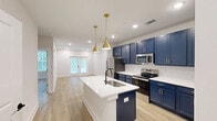 Located at 900 Corby Lane in Charleston, SC, this thoughtfully designed one-bedroom, one-bathroom residence offers a clean, modern aesthetic throughout its well-appointed single floor. Light wood-look plank flooring runs continuously through every room, creating a cohesive and airy feel.

The open-concept kitchen and living area serves as the heart of the home. The kitchen is a standout feature, showcasing bold navy blue shaker-style cabinetry accented with gold hardware, bright white quartz countertops, a central island with an undermount sink, stainless steel appliances, a classic white subway tile backsplash, and a statement gold pendant light. The adjoining living area is bright and open, with recessed lighting and French doors that invite natural light and provide access to an outdoor balcony with greenery views.

The bedroom is a comfortable retreat, featuring multiple windows with natural light, a ceiling fan, and access to a dedicated walk-in closet outfitted with wire shelving for practical organization. The bathroom continues the navy and gold design palette, offering a navy vanity with gold accents, a white countertop, and a separate water closet with a walk-in tiled shower. Clean white walls and consistent finishes throughout lend the entire space a fresh, move-in-ready character.