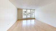 Located at 1905 NW 29th Ave in Portland, Oregon, this one-bedroom, one-bathroom unit offers an efficient and thoughtfully arranged floor plan. Light hardwood flooring runs throughout the space, lending warmth and continuity to each room.

The open living area is bright and clean-lined, featuring large floor-to-ceiling windows that flood the space with natural light and provide views of the surrounding streetscape. A second window orientation in the bedroom looks out onto a lush, landscaped green area with mature trees, a rolling lawn, and a stone-lined pathway — a standout feature that brings a peaceful, park-like quality to the unit.

The galley-style kitchen is well-equipped with light wood cabinetry, stainless steel appliances including a refrigerator, electric range, and dishwasher, paired with dark countertops and a single-basin sink — making efficient use of the available space.

The bedroom is a comfortable size, offering a closet and direct access to the serene garden view. Two closets total provide practical storage throughout the unit. The bathroom features a full soaking tub and shower combination with classic white tile and contrasting dark tile accents.

Textured ceilings and a clean, neutral color palette complete the interior, offering a simple and functional living environment in a verdant Portland neighborhood.