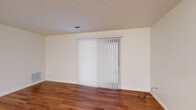 This single-floor unit offers a well-organized layout that balances functionality with comfort. The main living area is finished with warm hardwood-style flooring that extends throughout much of the space, complemented by neutral white walls and a textured ceiling. A large sliding glass door fitted with vertical blinds fills the living area with natural light and provides access to the outdoors.

The galley-style kitchen is efficiently designed with rich dark wood cabinetry lining both sides, granite-look countertops, a stainless steel sink, and white appliances including a refrigerator, electric range, and over-the-range microwave. The wood-look flooring continues seamlessly into the kitchen, maintaining a cohesive aesthetic.

The bedrooms are carpeted in a neutral beige tone, creating a softer, quieter environment. One bedroom features a spacious reach-in closet with double doors and a wire shelving system, offering ample storage. A secondary bedroom includes a window with blinds that brings in natural light.

A dedicated utility room houses the water heater, a utility sink, washer/dryer hookups, and wire shelving — a practical addition that adds significant convenience. Throughout the unit, HVAC vents are consistently placed for efficient climate control, and the overall layout, as seen in the dollhouse view, is compact yet thoughtfully arranged.