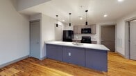 Located at 400 N Grove St in Hendersonville, NC, this single-floor loft-style space showcases a compelling blend of industrial heritage and contemporary updates. The living area is a standout, boasting soaring ceilings, exposed brick walls, and expansive multi-pane steel-framed windows that flood the interior with abundant natural light while offering views of the surrounding brick architecture. Original hardwood floors run throughout, adding warmth and continuity to every room.

The kitchen is well-appointed and available in two distinct configurations. One layout features a galley-style design with gray shaker cabinetry, granite countertops, and black appliances including a refrigerator, electric range, and over-the-range microwave. The second configuration opens to the living space via a large peninsula with a granite countertop, undermount sink, pendant lighting, and a subway tile backsplash, combining function with an open, social layout.

The bathroom is clean and modern, featuring granite countertops, an undermount sink with a wide vanity mirror, hardwood flooring, and a full tub-and-shower combination with chrome fixtures. The overall design of this space balances the raw character of its industrial roots with thoughtfully selected contemporary finishes.