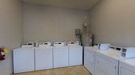 Located at 111 Springview Ln in Summerville, South Carolina, this single-floor laundry facility is designed to serve residents with practical, no-frills functionality. The room features a row of coin-operated top-loading washing machines lined along one wall, complemented by a set of commercial dryers, providing ample capacity to handle laundry needs efficiently. The space is finished with neutral gray walls and light tile flooring, creating a clean and low-maintenance environment. A water heater and utility panel are visibly housed within the room, reflecting the straightforward, utilitarian layout of the facility. Overhead lighting ensures the space is well-lit throughout. The layout is thoughtfully organized to allow easy access to each machine, making the laundry process as streamlined as possible. This communal laundry room offers a convenient, shared amenity ideally suited for residents seeking on-site laundry access without the need for in-unit machines.
