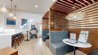 Located at 2726 Moorhead Ave in Boulder, CO, this single-floor leasing office is a thoughtfully designed space that blends modern aesthetics with functional comfort. Upon entry, visitors are greeted by soaring ceilings and large framed artwork that set an inviting, professional tone. A dedicated reception desk with a workstation sits adjacent to the entrance, providing a clear and organized point of contact.

The centerpiece of the space is a pair of striking slatted wood booth enclosures, each outfitted with channeled gray upholstered bench seating and petite round tables beneath woven pendant lights. These semi-private nooks offer an ideal setting for consultations or informal meetings, combining visual warmth with a sense of intimacy. The slatted wood detailing extends overhead, adding architectural depth and a natural aesthetic throughout.

A large skylight floods the central area with abundant natural light, enhancing the open and airy feel of the interior. Light-toned hardwood-style flooring runs throughout, further brightening the space.

The kitchenette is well-appointed with dark shaker-style cabinetry, a geometric tile backsplash, stainless steel appliances, a deep single-basin sink, and a generous white quartz island with bar stool seating — ideal for casual gatherings or staff use. Curated artwork and playful branded decor, including a bear mascot cutout, add personality and a distinctly Colorado character to this polished, welcoming office environment.