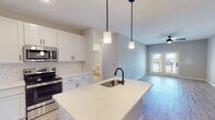 Located at 30101 Snowmass Loop in Garner, NC, this single-floor residence offers a thoughtfully designed open-concept layout with contemporary finishes throughout. The kitchen serves as a central highlight, showcasing crisp white shaker cabinetry, a geometric herringbone tile backsplash, light quartz countertops, and a center island with an undermount sink and matte black faucet. Stainless steel appliances, including a refrigerator, range, and over-the-range microwave, complete the space. Pendant lighting above the island and light wood-look flooring carry through seamlessly into the adjoining living area.

The living room is bright and open, featuring a ceiling fan, neutral walls, and French doors that lead to a private balcony with outdoor views. Bedrooms are carpeted for comfort, with ceiling fans, ample natural light, and walk-in closets with built-in shelving. The bathroom is finished with wood-look flooring, a white vanity, and a tub-shower combination accented by matte black hardware and fixtures. Consistent use of neutral tones, black hardware accents, and durable flooring materials gives the entire residence a cohesive, modern aesthetic.