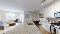 Located at 410 Princeton Road in Yaphank, NY, this single-floor residence at The Brio at The Boulevard showcases a thoughtfully designed open-concept layout that seamlessly connects the kitchen, dining, and living areas. Rich hardwood-style flooring runs throughout the main living spaces, complementing the bright, neutral color palette that gives the home a clean and contemporary feel.

The kitchen is a standout feature, equipped with stainless steel appliances including a gas range, microwave, and full-size refrigerator. Crisp white shaker cabinetry extends to the ceiling, offering generous storage, while granite countertops and a tiled backsplash add polished detail. A large kitchen island with a built-in sink and bar seating connects the kitchen to the dining and living areas. A dedicated dining space with a framed wall mirror provides a defined area for meals.

The living room is well-lit with multiple windows and French doors that open to a private patio, inviting natural light throughout. Bedrooms feature plush carpeting and closet storage, while the bathroom is appointed with granite-topped white cabinetry, a single vanity, and a full tub-shower combination. Track and flush-mount lighting add functional illumination throughout this well-appointed residence.