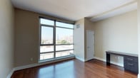 This contemporary single-floor residence offers a thoughtfully designed open layout with rich hardwood flooring that flows seamlessly throughout the living areas. The living space is anchored by expansive floor-to-ceiling windows that frame sweeping urban skyline views, flooding the interior with natural light and creating a strong visual connection to the city beyond. A dedicated closet provides convenient built-in storage directly off the main living area.

The kitchen is outfitted with dark espresso cabinetry, granite countertops, and a full suite of stainless steel appliances including a refrigerator, electric range, built-in microwave, and dishwasher. A classic subway tile backsplash adds a clean, modern aesthetic, while recessed lighting ensures excellent task illumination. The kitchen opens directly to the main living area, reinforcing the open-concept flow of the space.

The bathroom features large-format, textured tile surrounding a soaking tub and shower combination with a curved curtain rod. Granite countertop detailing and neutral tones lend a polished, cohesive finish. Throughout the residence, warm beige walls complement the deep hardwood floors, creating an inviting and contemporary ambiance suited for modern urban living.