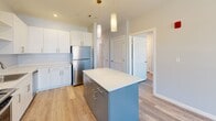 Located at 1 Royal Dr in Somersworth, New Hampshire, this thoughtfully designed 2-bedroom, 1-bathroom residence offers a clean, contemporary aesthetic across a single floor. Light gray walls, crisp white trim, and wood-style luxury vinyl plank flooring run throughout the space, creating a cohesive and modern atmosphere.

The kitchen serves as a central highlight, featuring white upper cabinetry, gray lower cabinets, a white countertop island with pendant lighting overhead, and a full suite of stainless steel appliances including a range, microwave, dishwasher, and refrigerator. The open layout connects seamlessly to the hallway, which provides easy access to both bedrooms.

Both bedrooms are well-proportioned and filled with natural light from large windows with exterior views of the surrounding community. The primary bedroom offers a comfortable footprint ideal for a full bedroom set. Each bedroom features the same durable hardwood-style flooring found throughout the home.

The bathroom is clean and functional, outfitted with tile flooring, a combination tub and shower, and a vanity with warm wood cabinetry and ample counter space. Additional storage is provided by a hallway closet. The overall design of this residence emphasizes modern simplicity, practical functionality, and a bright, welcoming ambiance.