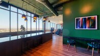 Sky Lounge is a sophisticated, high-rise amenity space designed to blend industrial aesthetics with refined comfort. Floor-to-ceiling windows wrap the perimeter, flooding the interior with abundant natural light and offering breathtaking panoramic views of the surrounding cityscape and beyond.

The space is anchored by a bold deep-green color palette, applied to the walls and structural columns, which contrasts striking exposed ductwork and concrete ceilings overhead. Warm hardwood flooring transitions throughout, complementing the layered textures of the interior.

A prominent bar counter with a dark, polished surface serves as a central gathering point, illuminated by a cluster of pendant lights with gold-toned interiors. Adjacent to the bar, a floor-to-ceiling built-in bookshelf, framed in the signature green, adds a library-inspired nook ideal for quiet retreat.

The lounge area features a curated mix of seating, including teal accent chairs, low-profile sofas, and bar-height seating, all arranged around a large flat-screen television. Patterned area rugs define conversation zones, while a chandelier adds a touch of warmth to the far entertaining area.

The entrance features bold green walls and classic double doors, creating a strong first impression. Throughout, carefully selected artwork and greenery enhance the overall ambiance, making Sky Lounge a dynamic and inviting space for socializing, relaxing, or working with a view.