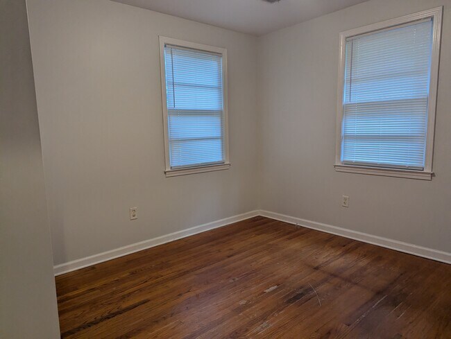 Dormitorio luminoso con paredes pintadas en tonos neutros, dos ventanas y suelo de imitación madera. - 1527 Brookbank Ave