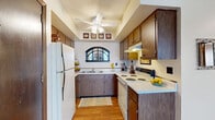 Located at 1600 W Bradley Ave in Champaign, Illinois, this 2-bedroom, 1-bathroom residence offers a well-organized single-floor layout designed for comfortable everyday living. The U-shaped kitchen features warm wood-toned cabinetry, white appliances including a refrigerator and electric range, light hardwood flooring, and a distinctive arched window above the sink that brings in natural light. A tray ceiling with a ceiling fan adds a subtle architectural touch to this functional cooking space. The living room is carpeted and comfortably sized, equipped with a wall-mounted mini-split HVAC unit and neutral walls that create a welcoming atmosphere. A dining nook adjacent to the living area provides additional flexibility for the space. Both bedrooms are carpeted and feature sliding-door closets and windows with blinds that allow for natural light and privacy. The primary bedroom is generously proportioned and offers direct sightlines to the bathroom. The full bathroom includes a tiled tub-and-shower combination with white tile surround and tile flooring. Throughout the unit, wood-trimmed doorways and baseboards provide consistent, classic detailing that ties the space together cohesively.