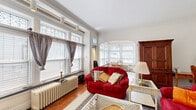 Located at 585 W Ferry St in Buffalo, NY, this well-appointed one-bedroom, one-bathroom unit blends classic architectural character with comfortable, functional living across a single floor. The spacious living room is entered through an elegant arched doorway and features original crown molding, hardwood floors, large windows that invite abundant natural light, and cast-iron radiators that speak to the building's historic charm. An arched opening connects the living room to the sun-drenched dining area, a standout bay alcove surrounded by large windows adorned with ornate leaded and stained glass transoms overhead, illuminated by a classic chandelier — an ideal spot for morning meals. The kitchen is equipped with warm-toned raised-panel wood cabinetry, a bold black tile backsplash, and full appliances including a dishwasher. The bedroom offers a quiet, carpeted retreat with a ceiling fan, track lighting, and ample space for a full furniture arrangement. The bathroom retains its period character with classic white subway tile wainscoting, a blue tile accent border, mosaic tile flooring, a pedestal sink, and a shower-tub combination. A connecting hallway ties the layout together efficiently, making this a cohesive and characterful urban residence.