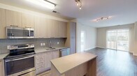 This well-appointed two-bedroom, two-bathroom unit at 650 Shillings St in Alexandria, Virginia offers a thoughtfully designed single-level layout with a contemporary aesthetic throughout. The open-concept kitchen serves as a central feature, showcasing light wood cabinetry extending to the ceiling, stainless steel appliances including a refrigerator, range, microwave, and dishwasher, and a textured tile backsplash. A kitchen island with a neutral countertop provides additional workspace and a natural transition into the living area. Rich hardwood-style flooring runs through the main living spaces, adding warmth and continuity. The living room is bright and airy, highlighted by a sliding glass door that opens to a private balcony with views of the surrounding area. The spacious primary bedroom offers generous proportions and comfortable carpet flooring, while the second bedroom is similarly finished and versatile. Both bathrooms are modern in design, with one featuring large-format floor tiles, white cabinetry, a framed mirror, and a tiled shower-tub combination. Neutral wall tones throughout create a clean, move-in-ready environment. A dedicated closet provides practical storage to complete this well-balanced unit.