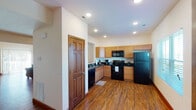 This well-appointed multi-floor residence spans three levels, offering a thoughtfully designed layout with consistent finishes throughout. The living room is a welcoming space featuring rich hardwood-style flooring, warm neutral walls, and a large sliding glass door fitted with vertical blinds that allows abundant natural light to fill the room. An architectural pass-through opening connects the kitchen directly to the dining and living areas, creating an open and social atmosphere. The kitchen is equipped with light maple cabinetry, dark granite countertops, black appliances including a refrigerator, range, microwave, and dishwasher, complemented by recessed lighting overhead. Adjacent to the kitchen, the dining area accommodates a round wooden table with ample seating, ideal for everyday meals or entertaining. Bedrooms are carpeted for comfort and feature windows that bring in natural light. The bathroom includes a warm wood vanity, tile flooring, and a well-lit mirror above the sink. Consistent six-panel wood doors and rich wood trim are found throughout the home, adding a cohesive, classic touch. The attached two-car garage provides generous parking and storage space. A central staircase connects all three floors, reinforcing the home's functional and spacious character.