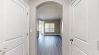 Located at Lenox Farms in Braintree, MA, this thoughtfully designed 2-bedroom, 1-bathroom apartment spans 1,130 square feet on a single floor. The open living room features crown molding, neutral gray walls, wood-look luxury vinyl plank flooring, and large windows with blinds that invite abundant natural light and tree-lined outdoor views. Elegant arched architectural details connect the living areas, adding a refined touch to the layout. The kitchen is equipped with stainless steel appliances including a range, over-the-range microwave, and refrigerator, complemented by white shaker cabinetry, white quartz countertops, and a classic subway tile backsplash. The primary bedroom measures 170 square feet and includes a ceiling fan and a dedicated walk-in closet with wire shelving for ample storage. The second bedroom also features large windows with views of the surrounding greenery. The full bathroom offers a tiled tub-and-shower combination, white shaker vanity with a framed mirror, and overhead cabinetry for additional storage. Wood-look flooring runs throughout the unit, tying the spaces together with a clean, modern aesthetic. The layout also includes an entrance, hallway, and staircase access.
