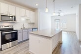 This well-appointed single-floor residence offers a bright and cohesive modern design throughout. The kitchen is a standout feature, showcasing white shaker cabinetry, granite countertops, a white subway tile backsplash, and a full suite of stainless steel appliances including a French door refrigerator with ice and water dispenser, electric range, over-the-range microwave, and dishwasher. A generous island with matching granite provides additional prep and gathering space, while pendant lighting and recessed fixtures illuminate the area. The kitchen opens seamlessly into the living area, which features light wood-look flooring, a ceiling fan with light, and a glass-paned door that invites natural light from outside. The bedrooms are finished with plush wall-to-wall carpet for comfort and include ample closet space. The bathroom is clean and contemporary, featuring a walk-in glass-enclosed shower, a granite-topped vanity, and wood-look tile flooring. A dedicated laundry room accommodates a full-size top-loading washer and dryer with overhead wire shelving for added storage. Throughout the home, a neutral white and light grey palette creates a fresh, airy ambiance ideal for a variety of interior styles.
