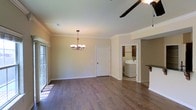 This two-story home offers a well-designed layout that balances comfort and functionality. The main living area is finished with rich hardwood flooring that extends throughout, adding warmth and a sense of continuity to the space. Crown molding lines the ceilings, lending a classic, refined character to the interior. An elegant chandelier anchors the dining or living area, while a ceiling fan provides practical comfort in an adjoining space. Large windows allow natural light to pour in, brightening the neutral-toned walls and creating an open, airy atmosphere. A dedicated laundry area is conveniently accessible from the main living space, complete with cabinetry and shelving for organized storage. A breakfast bar or counter ledge nearby hints at a connected kitchen, suggesting a seamless flow between the home's key gathering areas. Interior doors are finished in a clean, traditional panel style that complements the overall aesthetic. Across its two floors, this home presents a cohesive design rooted in classic architectural details, making it a welcoming and well-appointed residence suited for everyday living.