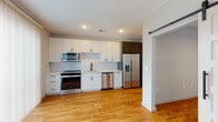 This contemporary single-floor unit is thoughtfully designed with a clean, modern aesthetic and consistent finishes throughout. Warm hardwood flooring flows seamlessly across all main living areas, connecting each space with a cohesive and inviting feel.

The kitchen serves as a functional centerpiece, outfitted with a full suite of stainless steel appliances including a range, over-the-range microwave, dishwasher, and a French door refrigerator with an ice and water dispenser. Crisp white shaker cabinetry with dark hardware lines the walls, complemented by a classic white subway tile backsplash and light countertops. A sliding barn-style door adds a stylish touch at the kitchen entrance. A large sliding glass door floods the area with natural light and opens to an outdoor view of the surrounding urban streetscape.

A well-proportioned hallway with recessed lighting leads through the unit, offering a smooth transition between spaces. The bedroom is bright and airy, featuring a large window with views of the neighboring architecture, a ceiling fan, and a spacious walk-in closet with built-in shelving.

The bathroom is finished with large-format gray floor tiles and a full soaking tub enclosed by white subway tile walls and accented with matte black hardware and fixtures, delivering a sharp, contemporary look throughout.