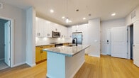 Located at 1650 Clearwater Largo Rd in Largo, Florida, this single-floor residence showcases a contemporary design with a clean, modern aesthetic throughout. The open-concept layout seamlessly connects the kitchen and living area, creating a spacious and functional environment ideal for everyday living.

The kitchen is a standout feature, centered around a large island with granite countertops and an undermount sink with a matte black faucet. Upper cabinetry is finished in crisp white, complemented by warm wood-toned lower cabinets with black hardware. Stainless steel appliances, including a French door refrigerator, electric range, and built-in microwave, complete the space. Pendant lighting and recessed ceiling lights provide layered illumination throughout.

The living area extends from the kitchen with light-toned hardwood flooring underfoot and a ceiling fan overhead. Natural light filters in through multiple windows fitted with blinds. The bedrooms feature neutral-toned carpet and generous windows that bring in additional natural light.

The bathroom maintains the unit's modern palette, featuring a wood-toned vanity with granite countertop, a tub-shower combination with white tile surround, and matching hardwood-style flooring, creating a cohesive and polished finish throughout the home.