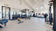 Located at 156 West Fairway Lane in Fort Collins, Colorado, this fitness center offers a thoughtfully designed workout facility spread across a single floor. The space is divided into two distinct areas, each tailored to different training styles.

The main gym area impresses with soaring vaulted ceilings that lend an open, airy atmosphere. Crisp white walls and an abundance of natural light from large windows along multiple sides of the room create a bright and energizing environment. The durable speckled rubber flooring throughout the main floor provides both safety and comfort. The space is comprehensively outfitted with a full rack of dumbbells, a power rack with barbells and weight plates, cable machines, adjustable benches, a stair climber, treadmills, and additional selectorized strength equipment. A wall-mounted television and storage cubbies for personal belongings add to the practicality of the space.

A separate studio room features light hardwood flooring and expansive floor-to-ceiling mirrors that visually amplify the space. This room is equipped with interactive cycling bikes and stability balls, making it ideal for group fitness or solo cycling sessions. Natural light pours in through large windows, contributing to an inviting and motivating atmosphere. Together, the two areas form a comprehensive, modern fitness facility well-suited for a full range of workout routines.