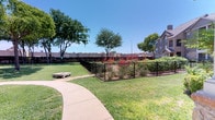 This thoughtfully designed community garden offers a welcoming outdoor retreat filled with lush greenery, colorful blooms, and productive growing spaces. A winding flagstone pathway serves as the central spine of the garden, guiding visitors through a curated landscape of raised wooden planting beds brimming with vegetables, ornamental grasses, and flowering plants. Vibrant red blooms — including striking red yucca stalks and crepe myrtles — add bold pops of color throughout the space, creating a visually dynamic environment across all seasons.

The garden is divided into distinct zones: cultivated raised beds lined with timber borders sit alongside decorative gravel and stone-accented plantings, offering both functional growing areas and ornamental appeal. Scattered seating, including wooden benches and a concrete rest area, provide comfortable spots for visitors to pause and enjoy the surroundings. Mature shade trees are positioned throughout, offering natural relief from the sun.

A sturdy decorative iron fence encloses the entire garden, providing definition and security while maintaining open sightlines to the surrounding landscape. An adjacent open lawn area complements the garden, adding generous green space for relaxation. The combination of native plantings, structured layout, and thoughtful amenities makes this community garden an inviting and functional shared outdoor space.