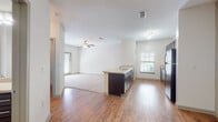 This single-story residence features a thoughtfully designed open-concept layout that seamlessly connects the kitchen and living areas. Wood-look flooring runs throughout the main living and kitchen spaces, creating a warm, cohesive aesthetic, while plush neutral carpet defines the spacious living room area, which is equipped with a ceiling fan and benefits from natural light through blinds-fitted windows.

The kitchen is well-appointed with rich, dark espresso cabinetry accented by brushed nickel hardware, light-toned countertops, and a full suite of stainless steel appliances including a refrigerator, electric range, and built-in microwave. A kitchen island with a sink and matching dark cabinetry adds both functionality and additional workspace, serving as a natural divider between the kitchen and living areas. A window above the counter allows natural light to fill the cooking space.

The bathroom continues the consistent design language with dark vanity cabinetry, a light countertop, a single undermount sink, a large mirror, and wood-look flooring. A full tub and shower combination with built-in shelving and a tiled surround completes the space. Overall, the unit maintains a clean, neutral palette throughout, lending itself to a bright and functional living environment.