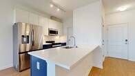 Located at 200 Townsfolk Alley in Penfield, NY, this thoughtfully designed one-bedroom, one-bathroom unit offers a clean, modern aesthetic throughout its efficiently utilized single-floor layout. The entry foyer welcomes residents with light wood-style flooring, crisp white walls, and a smart keypad-equipped door, setting a contemporary tone from the moment of arrival. The open-concept kitchen is a standout feature, boasting a bold navy blue island with a white quartz countertop and an undermount sink, contrasted by white upper cabinetry and stainless steel appliances including a French door refrigerator, built-in microwave, and range. Track lighting illuminates the space effectively, enhancing the modern, clean design. The living area flows naturally from the kitchen, continuing the light wood-style flooring. The bedroom offers a comfortable and quiet retreat with plush carpeting, bright white walls, and a large window that frames pleasant outdoor views and allows ample natural light. A dedicated closet provides convenient storage. The bathroom features the same light flooring found throughout the common areas, a sleek navy vanity with white countertop, a large mirror, and chrome fixtures, maintaining the home's cohesive modern style throughout.