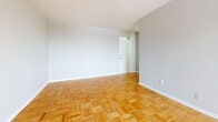 This 1-bedroom, 1-bathroom unit offers a practical and comfortable layout across a single floor. Classic light-toned parquet wood flooring runs throughout the living areas and bedroom, lending warmth and a timeless aesthetic to the space. The open living room is bright and airy, benefiting from a large floor-to-ceiling window and a glass balcony door that invites natural light and provides access to outdoor views. A baseboard heating unit is positioned beneath the window, ensuring year-round comfort. The kitchen is designed as a galley-style space, equipped with white cabinetry, a grey tile backsplash, dark countertops, a double sink, and white appliances including a refrigerator and electric range. Light ceramic tile flooring grounds the kitchen area. The bedroom is a comfortable size, featuring the same warm parquet flooring, a built-in closet with sliding doors, and a window with natural light and a radiator beneath it. The bathroom is finished with elegant marble-style large-format wall tiles surrounding the soaking bathtub, complemented by a wood-toned vanity with a white countertop. The overall ambiance of the unit is clean, neutral, and move-in ready.