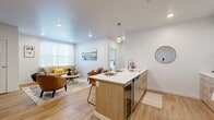 This thoughtfully designed one-bedroom, one-bathroom residence features a contemporary open-concept layout that seamlessly connects the kitchen, dining, and living areas. The kitchen is a functional centerpiece, boasting a wood-toned island with a white quartz countertop and bar seating, white upper cabinetry, complementary lower cabinets, a classic subway tile backsplash, and a full suite of stainless steel appliances including a refrigerator, range, and microwave. Light wood-style flooring flows throughout the main living areas, enhancing the bright, airy ambiance created by recessed lighting and large windows dressed with plantation shutters. The living room offers a comfortable, well-lit retreat with natural light streaming in through oversized windows. The bedroom features plush carpeting, a ceiling fan, and dual windows that invite natural light, while the dedicated closet provides practical storage. The bathroom is finished with warm wood-tone cabinetry, a white quartz vanity countertop, open shelving, a tub-shower combination with marble-style tile surround, and wood-look tile flooring. Clean white walls and modern fixtures tie the entire residence together in a cohesive, contemporary aesthetic.