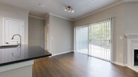 This single-floor unit is designed with a cohesive neutral palette and a thoughtful layout that balances comfort and functionality. The living area is a standout space, anchored by a classic white-mantled fireplace and rich wood-look flooring that extends throughout the main areas. Crown molding adds a refined architectural detail to the ceiling, while a sliding glass door fitted with vertical blinds opens to a balcony overlooking lush greenery, filling the room with natural light.

Adjacent to the living area, the dining space benefits from the same warm flooring and a track lighting fixture overhead. A dark-topped kitchen counter provides a visual contrast to the otherwise light and airy design. The kitchen is well-appointed with white cabinetry, a dark glass tile backsplash, grey countertops, and a full suite of stainless steel appliances including a range, over-the-range microwave, and dishwasher.

The bedrooms are carpeted for comfort and include ceiling fans with light fixtures and natural light from windows. The primary bedroom connects directly to a bathroom featuring a soaking tub, dark-topped vanity with white cabinetry, and wood-look flooring. A generously sized walk-in closet with wire shelving on multiple walls provides substantial storage. Additional carpeted rooms offer flexible living options throughout the unit.