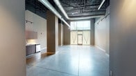 Located at 911 Locust Street in downtown St. Louis, Missouri, this first-floor unit offers a compelling blend of industrial character and modern finishes. The open main area immediately impresses with its soaring ceilings, exposed ductwork, and dark-painted structural elements that contrast cleanly against neutral-toned walls. Polished concrete floors extend throughout the entire unit, providing a sleek, durable surface that enhances the loft-inspired aesthetic.

Track lighting is installed throughout, offering flexible, directed illumination across all areas. A large street-facing window with sheer curtains draws in natural light, creating a bright and welcoming atmosphere in the main living area. A structural column anchors the central space, contributing to the industrial character without interrupting the overall flow.

A kitchenette is tucked neatly along one wall, featuring wood-toned cabinetry, a countertop workspace, and a stainless steel appliance, offering functional utility within the open-plan layout. A hallway leads to additional private rooms, each with tall ceilings and track lighting. These rooms include sliding panel doors that open to built-in shelving, providing organized storage solutions.

The bathroom is finished with large-format tile surrounds in the tub/shower area, a marble-topped vanity on a metal frame, and polished concrete flooring that maintains design consistency throughout the unit.