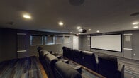 Located at 3500 Beaver Place Rd in Lexington, KY, this dedicated home theater room delivers a true cinematic experience within a single-floor layout. The space is designed with careful attention to both function and atmosphere, finished throughout in deep charcoal-gray walls that minimize light reflection and enhance on-screen contrast.

At the heart of the room is a large wall-mounted projection screen paired with a ceiling-mounted projector, creating a bold focal point for the viewing area. Seating is arranged in two tiered rows of plush black leather recliner chairs, each equipped with built-in cup holders — mirroring the comfort and layout of a professional movie theater. The elevated rear row ensures unobstructed sightlines from every seat.

The flooring features a striking multi-tone plank pattern in shades of blue, gray, and brown, adding visual depth to the room's otherwise dark palette. Recessed ceiling lighting provides ambient illumination, while blackout roller shades on the windows allow for complete light control during screenings. Acoustic panels are mounted along the side walls to optimize sound quality and reduce echo.

A dedicated exit door and emergency lighting underscore the room's thoughtful, venue-style design. This space is well-suited for private screenings, sports viewing, or entertainment gatherings.