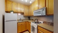 Located at 580 N Park St in Columbus, Ohio, this single-floor unit offers a practical and well-organized layout suited for comfortable everyday living. The kitchen is efficiently designed with warm honey-toned wood cabinetry extending to the ceiling, providing ample storage space. It features light-toned countertops, a stainless steel sink, a gas range with overhead microwave, and a full-size refrigerator, all set atop classic tile flooring. Crown molding details add a refined touch throughout the living areas, which are finished with neutral-toned carpet that lends a warm, cozy feel underfoot. The living space is open and versatile, with a straightforward entry foyer featuring tile flooring that transitions into the carpeted main area. A window fitted with horizontal blinds allows natural light to filter in, brightening the interior. The bathroom is clean and functional, featuring a tiled tub-and-shower combination, a white vanity with storage, a medicine cabinet mirror, and tile flooring. Neutral wall tones throughout the unit create a cohesive, understated palette that is move-in ready and easy to personalize.