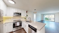 This well-appointed single-floor residence showcases a clean, modern aesthetic with thoughtful updates throughout. The kitchen is a standout feature, boasting crisp white shaker cabinetry, light quartz countertops, a classic subway tile backsplash, and a full suite of stainless steel appliances including a range, over-the-range microwave, dishwasher, and refrigerator. A peninsula with an undermount sink and a stylish ring pendant light above creates a natural connection to the adjacent living and dining area, making the space ideal for both everyday living and entertaining. The open living area is bright and airy, featuring hardwood-style flooring, white walls, and a sliding glass door that welcomes abundant natural light and provides access to an outdoor area with greenery views. A ceiling fan adds comfort to this versatile space. The bedroom is generously sized, offering mirrored sliding closet doors that enhance the sense of space, a ceiling fan with light, and wide windows fitted with white blinds that allow soft, diffused light to filter in. Hardwood-style flooring runs consistently throughout the residence, contributing to a cohesive and polished look. The overall ambiance is light, clean, and move-in ready, with modern finishes that balance style and practicality.