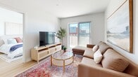 Located at Place de la Triade in Pointe-Claire, Quebec, this well-appointed 3-bedroom, 2-bathroom residence offers a thoughtfully designed single-floor layout with a clean, contemporary aesthetic throughout. The open-concept kitchen is a standout feature, boasting a large quartz waterfall island with bar seating, crisp white lower cabinetry paired with warm natural wood upper cabinets, a subway tile backsplash, and stainless steel appliances. Light hardwood flooring flows seamlessly through the main living areas, enhancing the bright and airy atmosphere. The living room is filled with natural light from a large sliding glass door that opens to an outdoor balcony, offering views of the surrounding area. The bedrooms are comfortably sized, with the primary bedroom featuring a generous window that invites abundant natural light. Both bathrooms are finished with large-format tile flooring — one includes a soaking tub and glass shower enclosure, while the second offers a streamlined vanity with warm wood cabinetry and white countertop. A dedicated in-unit laundry room houses side-by-side Whirlpool front-load washer and dryer units with overhead shelving, adding practical convenience. The overall design is modern and cohesive, with a neutral palette that creates a calm, welcoming ambiance throughout.