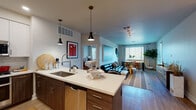 This thoughtfully designed single-floor residence showcases a seamless open-concept layout that connects the kitchen, living, and dining areas into one cohesive, functional space. The kitchen is a standout feature, equipped with stainless steel appliances including a gas range, microwave, and dishwasher, complemented by two-tone cabinetry — white upper cabinets and rich wood-toned lower cabinets — and a white quartz countertop island with pendant lighting overhead. A second kitchen configuration features a bold blue island with bar seating, offering a stylish alternative layout.

The living area is bright and welcoming, with natural light streaming through large windows fitted with blinds and curtains. Wood-style flooring flows throughout the main living spaces, while a dedicated dining nook comfortably accommodates a full dining table set.

Two well-sized bedrooms each feature ceiling fans, natural light from large windows, and neutral tones that create a calm retreat. The primary bathroom offers a dual-sink vanity with white cabinetry, and leads to a walk-in closet, while the secondary bathroom features a single vanity with clean, modern finishes. The overall design is contemporary and cohesive, balancing practicality with refined aesthetic details.
