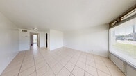 Located at 3870 N Andrews Ave in Oakland Park, FL, this single-story, one-bedroom, one-bathroom unit offers a practical and well-organized layout across a compact but efficiently designed floor plan. The living room is bright and open, featuring large windows that frame outdoor greenery and allow abundant natural light to fill the space. Light-toned ceramic tile flooring runs throughout the main living and kitchen areas, lending a clean, cohesive look. Two hallways connect the rooms, with three closets providing generous storage throughout. The kitchen is a galley-style space equipped with dark wood cabinetry, granite-look countertops, a stone tile backsplash, a stainless steel sink, and white appliances including a range and refrigerator. The bedroom offers a warm contrast with rich hardwood flooring and a floor-to-ceiling window dressed with vertical blinds, providing both natural light and privacy. The bathroom features a full tub-shower combination with white tile surround and clean white fixtures. A private patio extends the living space outdoors, offering a dedicated area for relaxation. The unit's textured ceilings and white walls throughout maintain a bright, neutral palette ideal for personalizing.