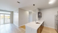 Located at 34 Jerome Ave in Bloomfield, CT, this thoughtfully designed single-floor residence offers three bedrooms and two full bathrooms with a cohesive modern aesthetic throughout. The open-concept kitchen and living area serves as the heart of the home, anchored by a sleek peninsula with a crisp white quartz countertop, an undermount sink, and a statement linear pendant light. The kitchen features dark wood cabinetry, stainless steel appliances, a tile backsplash, and light hardwood-style flooring that extends into the living area. The living room is bright and airy, enhanced by a sliding glass door that opens to a balcony and allows natural light to fill the space. The bedrooms offer a calm retreat; the carpeted rooms provide comfort underfoot, while one bedroom features hardwood-style flooring. Each bedroom includes closet space and windows with outdoor views, including seasonal foliage. The two bathrooms are finished with warm wood-toned vanities and white quartz countertops. One bathroom includes a soaking tub with a curved shower rod, while the second offers a well-lit vanity with a large mirror and a natural light-filled window. Clean lines and neutral tones unify the entire residence.