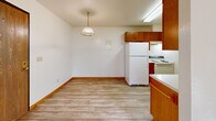 Located at 2517 Goettens Way in Saint Cloud, Minnesota, this single-floor unit offers a practical and well-organized layout designed for comfortable everyday living. The kitchen is equipped with warm honey-toned wood cabinetry extending to the upper walls, white appliances including a full-size refrigerator and range, a stainless steel sink, and light vinyl plank flooring. A skylight overhead brightens the space naturally. Adjacent to the kitchen is a dining area with a pendant light fixture and additional cabinetry, providing a convenient space for meals. The living area is spacious and carpeted, featuring a sliding glass door with vertical blinds that opens to an outdoor patio, allowing for natural light and exterior access. A wall-mounted air conditioning unit and baseboard heating ensure year-round climate comfort. The bedrooms are also carpeted and filled with natural light through blinds-fitted windows, with warm wood door and trim accents throughout. The bathroom includes a full tub and shower combo with a sliding glass enclosure, a wood-vanity with a single sink, and easy-to-maintain vinyl plank flooring that ties the space together. Textured ceilings and warm wood trim are consistent throughout, giving the unit a cohesive, functional character.