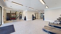 Located at 3450 Miller Dr in Chamblee, Georgia, this well-appointed fitness center offers a thoughtfully designed, single-floor layout that maximizes functionality and comfort. The expansive exercise room is the heart of the facility, featuring plush carpet flooring, crown molding, and bright recessed linear lighting that creates a clean, energizing atmosphere. The cardio section is equipped with multiple treadmills, an elliptical, and a stationary bike, all positioned near large floor-to-ceiling glass doors that flood the space with natural light and provide direct views of — and access to — an outdoor pool area. The strength and training zone houses a punching bag, weight bench, dumbbell rack, resistance machines, and various functional fitness accessories mounted on a dedicated wall rack, offering a comprehensive workout experience. Two restrooms serve the facility, each finished with light hardwood-style flooring, neutral gray walls, crown molding, and modern fixtures. The women's restroom includes an ADA-accessible design with a wall-mounted sink and paper towel dispenser. A tastefully decorated secondary restroom adds a refined touch with abstract wall art and a stylish wood-and-charcoal storage cabinet. Connecting hallways provide smooth circulation throughout the space, contributing to an overall ambiance that is clean, modern, and welcoming.