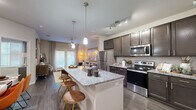 This thoughtfully designed single-floor residence offers an efficient and stylish open-concept layout that seamlessly connects the kitchen, dining, and living areas. The kitchen is a standout feature, equipped with dark espresso cabinetry, granite countertops, a full suite of stainless steel appliances, and a center island with pendant lighting and bar seating — ideal for both cooking and casual dining. Track lighting overhead adds a modern, functional touch throughout. Hardwood-style flooring runs throughout the main living areas, lending a cohesive and polished look. The living room is bright and welcoming, benefiting from large windows that allow ample natural light, complemented by a ceiling fan for comfort. The bedroom is a comfortable retreat, featuring large windows, a ceiling fan, and a barn-door-style headboard wall detail that adds a distinctive architectural character. The bathroom offers dual sinks set in a granite vanity with dark cabinetry and a large mirror, directly accessible from the bedroom. A dedicated closet provides convenient storage. The overall design balances contemporary finishes with warm, inviting tones throughout.