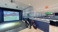 Located at 325 Huguenot St in New Rochelle, NY, this expansive single-floor facility offers a thoughtfully designed indoor golf and social experience spanning a generous footprint. The space is defined by its modern aesthetic, featuring light hardwood flooring, recessed lighting, and a cohesive navy and white color palette throughout.

At the heart of the facility is a full golf simulator bay, equipped with a large projection screen and real turf hitting surface, accommodating multiple golf bags and clubs. Adjacent to the simulator is a spacious putting green with multiple holes, artificial turf, and large floor-to-ceiling windows that flood the area with natural light and offer sweeping urban views.

A long bar-height counter with white marble surfaces and pendant lighting runs along one wall, accompanied by high seating and wall-mounted monitors — ideal for viewing and socializing. Nearby, a more relaxed lounge area features plush seating with green accent cushions, a zebra-print area rug, and additional floor-to-ceiling glazing that frames city views.

The open-plan layout connects all zones seamlessly, with light-filled corridors and intimate seating nooks positioned throughout. Colorful wall art and curated furnishings add personality to the space, creating an inviting atmosphere that balances active recreation with comfortable social gathering.