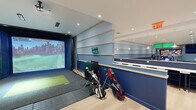 Located at 325 Huguenot St in New Rochelle, NY, this expansive single-floor facility offers a thoughtfully designed indoor golf and social experience spanning a generous footprint. The space is defined by its modern aesthetic, featuring light hardwood flooring, recessed lighting, and a cohesive navy and white color palette throughout.

At the heart of the facility is a full golf simulator bay, equipped with a large projection screen and real turf hitting surface, accommodating multiple golf bags and clubs. Adjacent to the simulator is a spacious putting green with multiple holes, artificial turf, and large floor-to-ceiling windows that flood the area with natural light and offer sweeping urban views.

A long bar-height counter with white marble surfaces and pendant lighting runs along one wall, accompanied by high seating and wall-mounted monitors — ideal for viewing and socializing. Nearby, a more relaxed lounge area features plush seating with green accent cushions, a zebra-print area rug, and additional floor-to-ceiling glazing that frames city views.

The open-plan layout connects all zones seamlessly, with light-filled corridors and intimate seating nooks positioned throughout. Colorful wall art and curated furnishings add personality to the space, creating an inviting atmosphere that balances active recreation with comfortable social gathering.